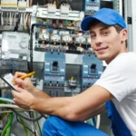 Ein Elektriker, der ein vor einem Sicherungskasten sitzt und Werte auf einem Block notiert