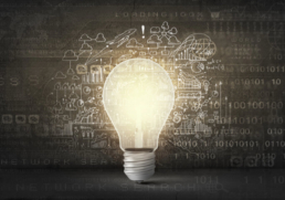 Eine leuchtende Glühbirne vor Wand mit technischen Zeichnungen